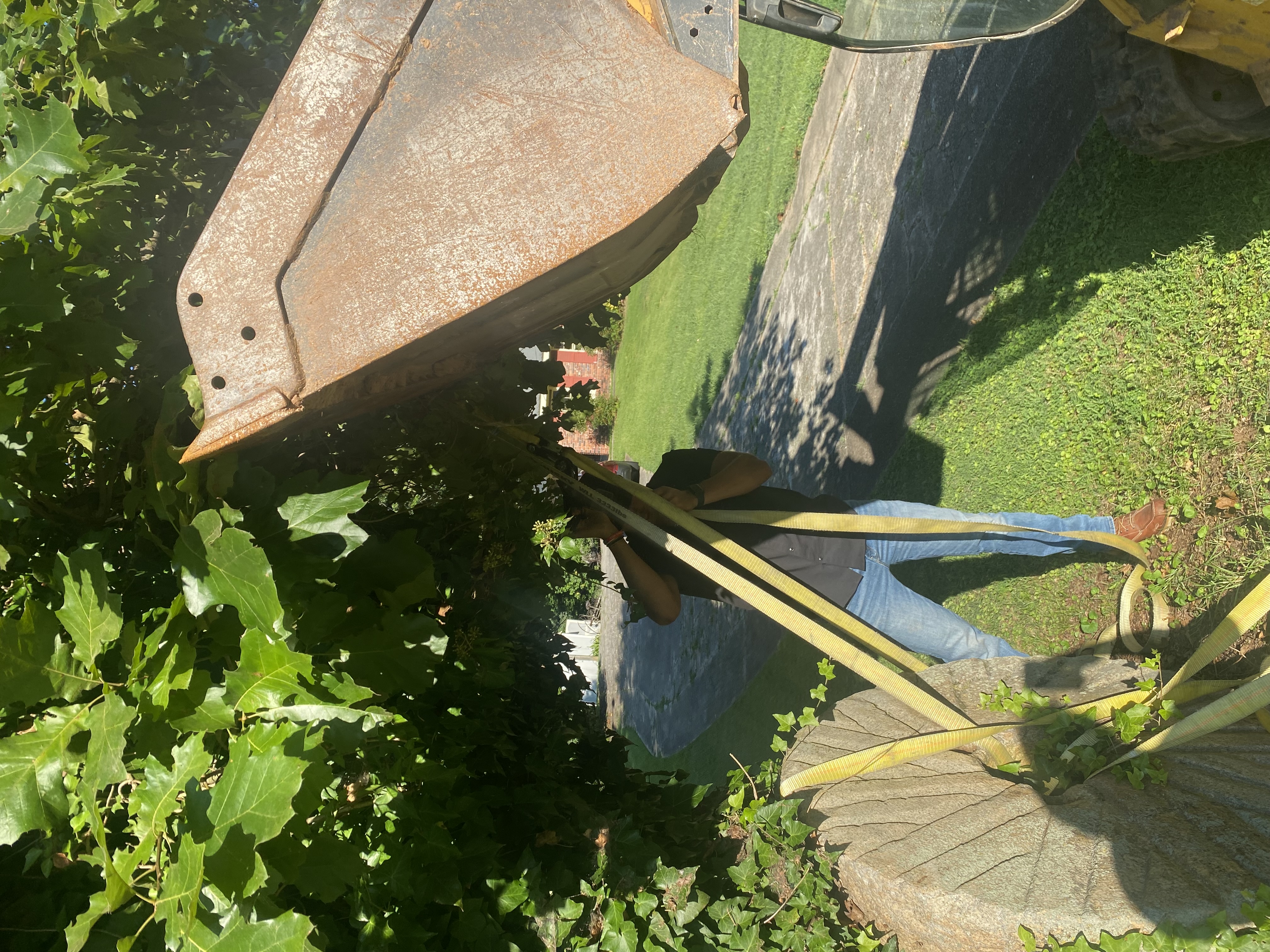 Haul Pro Hauling crew using a skid steer and lifting straps to move a heavy stone boulder
